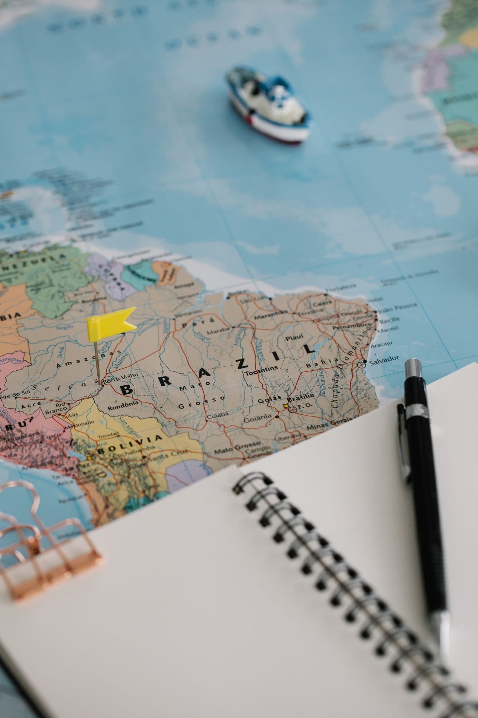 A travel map with a marker placed on Brazil beside a planning notebook