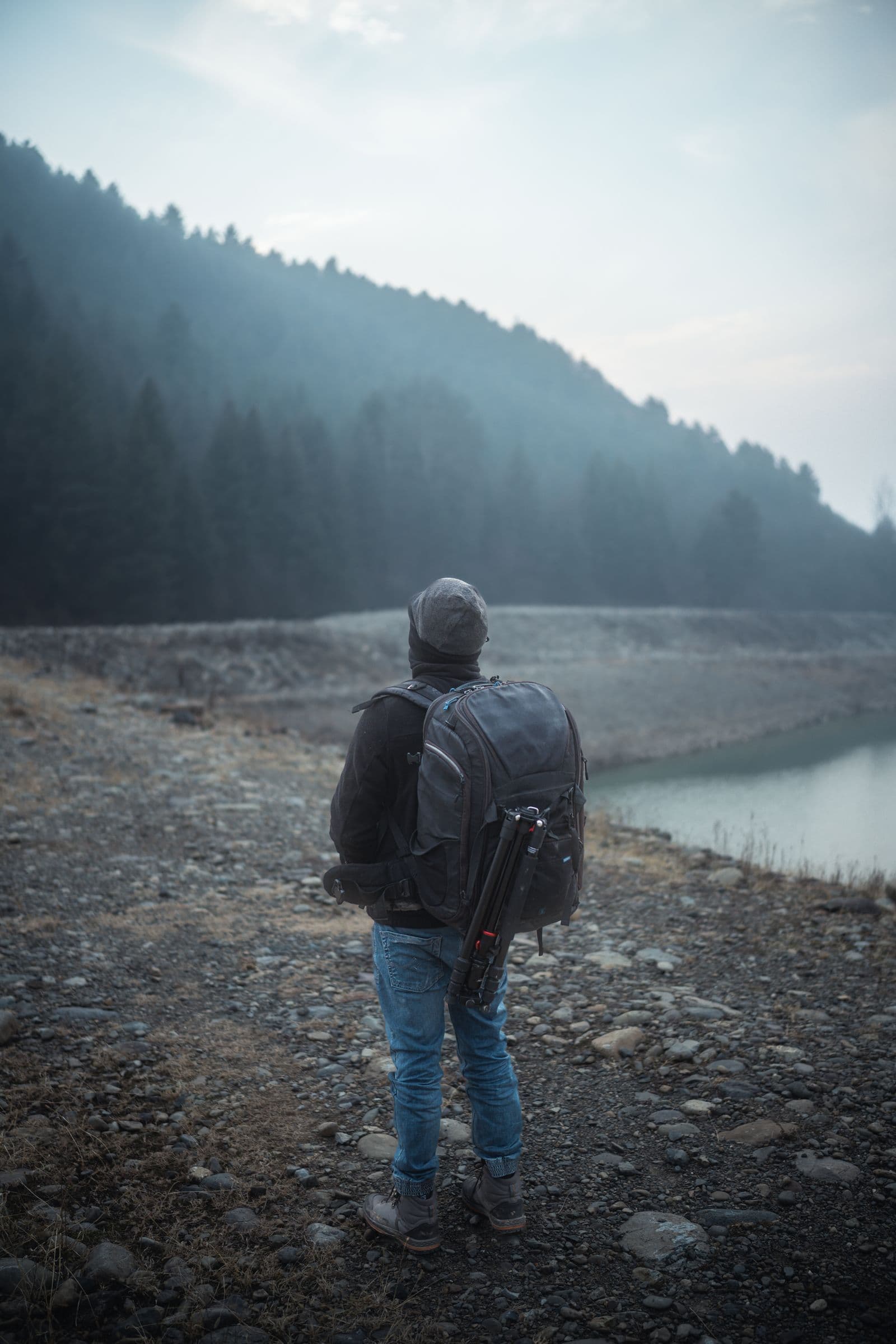 A solo traveler with a backpack looking across a mountain lake